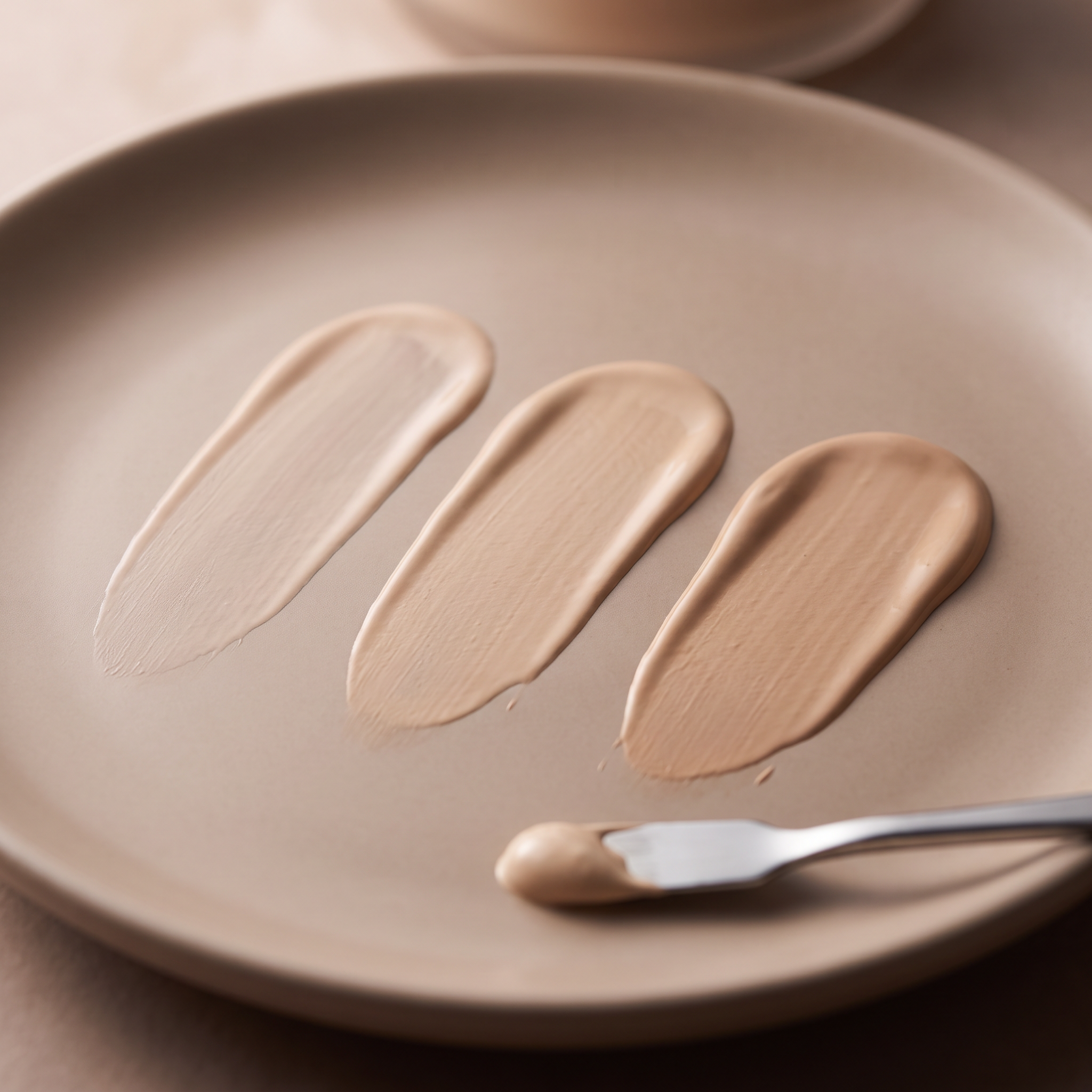 BB cream shade range arranged from very light to deep brown on a taupe surface