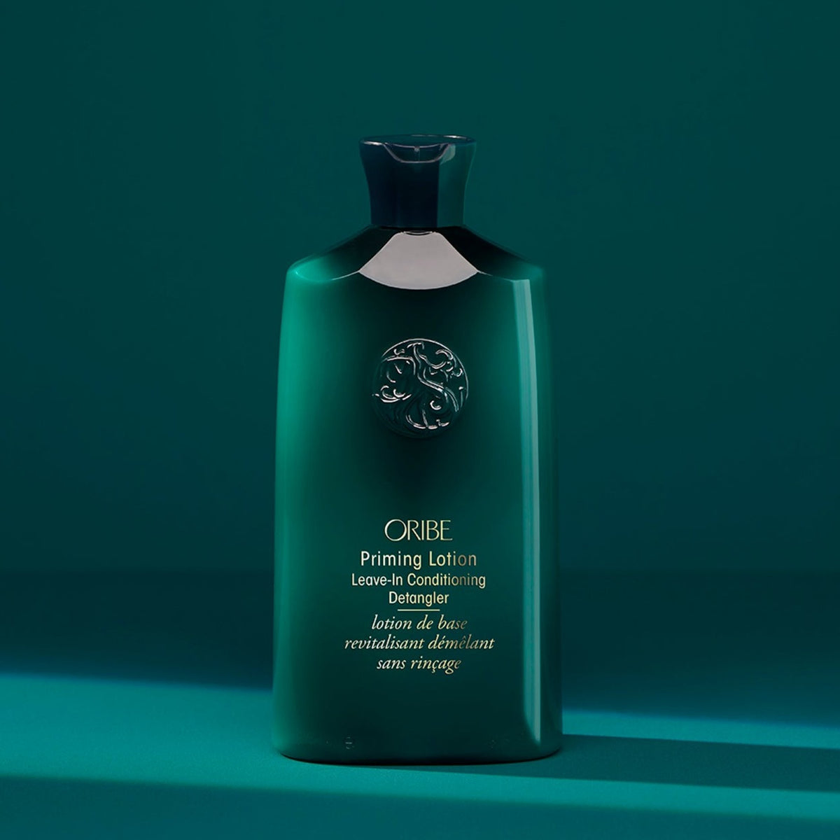Oribe Priming Lotion Leave-In Conditioning Detangler green bottle on a teal editorial background.